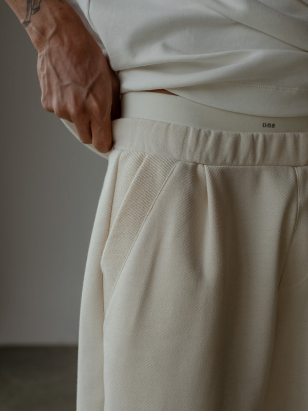 Detalle de la mano de modelo en la cintura enresortada del jogger color crema con bolsillos laterales, usando camiseta oversized color crudo.