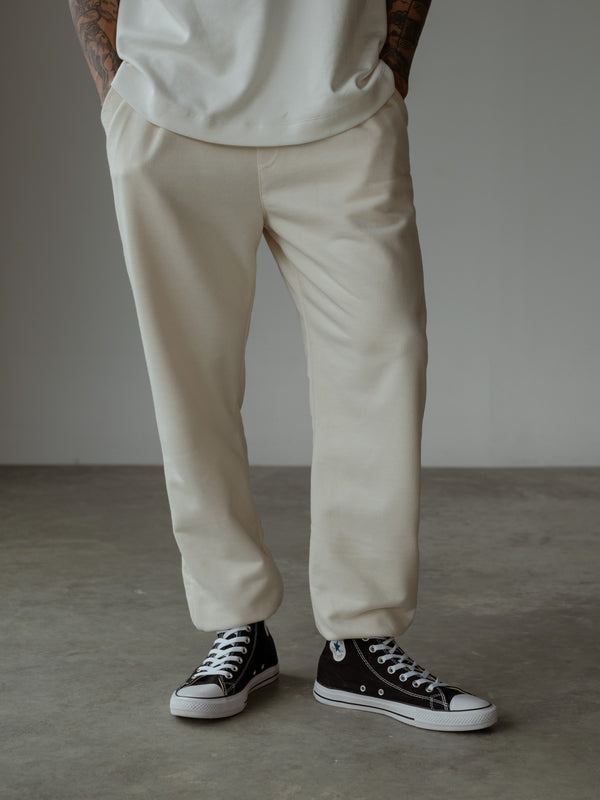 Primer plano de modelo de pie, usando jogger color crema con cintura enresortada y bota elástica, y camiseta oversized color crudo.