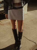Modelo usando mini falda plata con cinturón negro, crop top y botas.