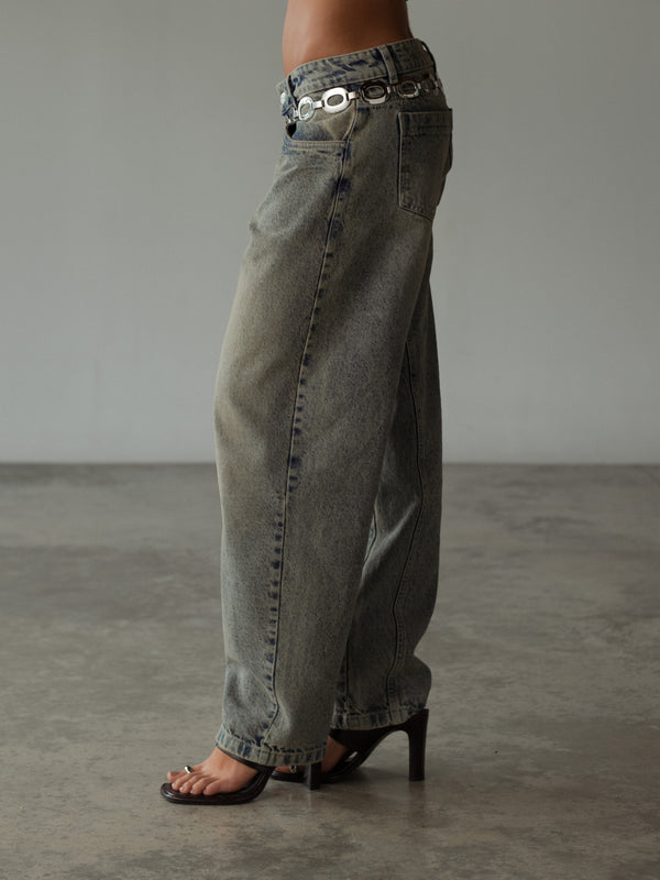 Vista lateral modelo con jean bota ancha con cinturón metálico.