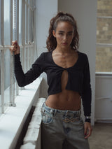 Modelo al lado de una ventana usando jean claro y top de nudo negro.
