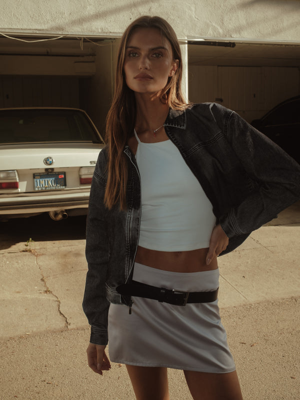 Vista frontal modelo con chaqueta, crop top halter crudo y mini falda satín.