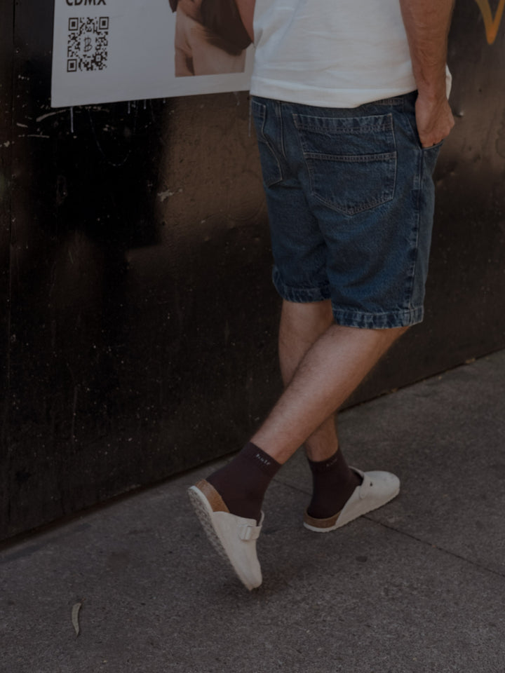 Modelo caminando mientras tiene una pantaloneta en denim azul con bolsillos posteriores y camiseta de algodón color crudo