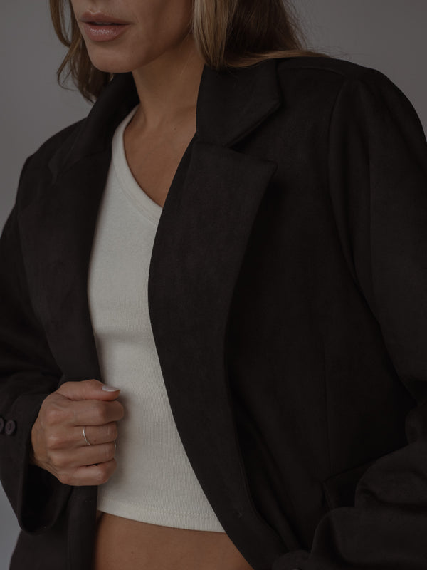 Primer plano de una modelo con un top asimétrico color crema bajo un blazer color negro.