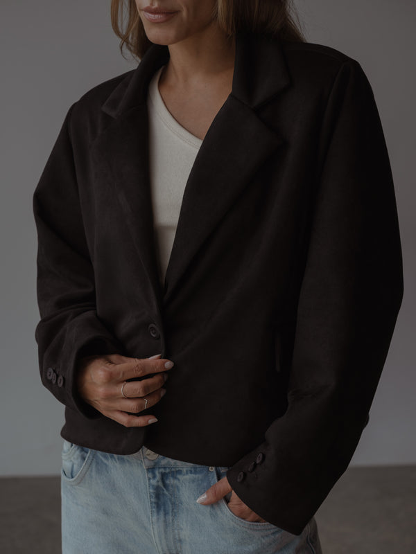 Mujer abrochando un blazer color negro, dejando ver un top color crema y un jean azul claro.