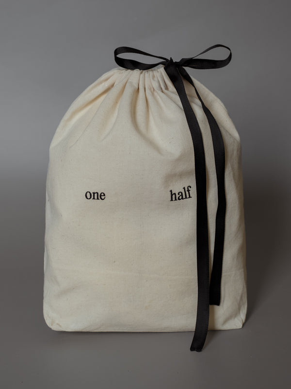 Bolsa de regalo de tela beige con moño negro y estampado "One Half" en negro. 
