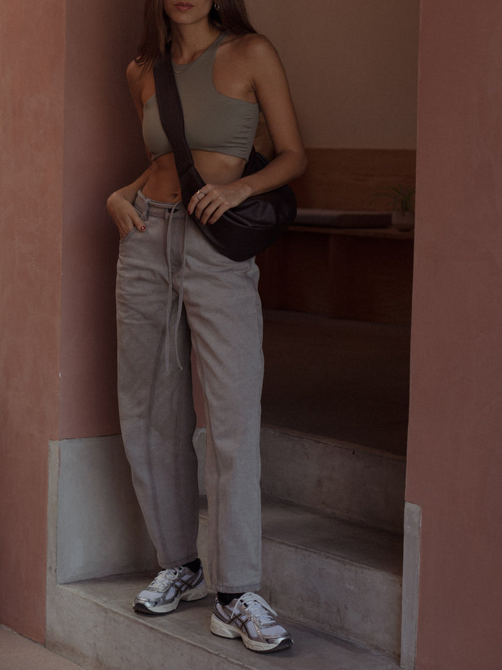 Modelo usando jean y crop top color gris con un bolso color café y tenis