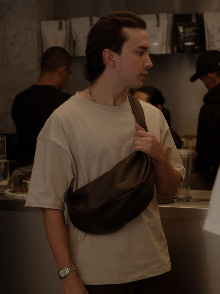 Modelo usando una camiseta color arena y un croos bag color café