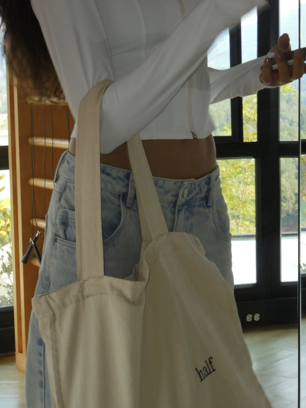 Modelo de pie con un bolso color crema con texto negro "half"