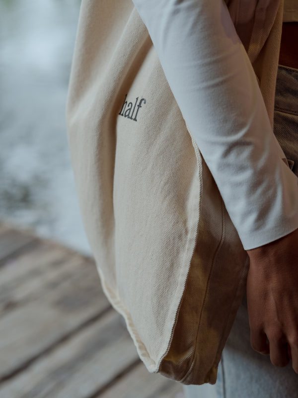Detalle lateral de un bolso color crema con texto negro "half"  