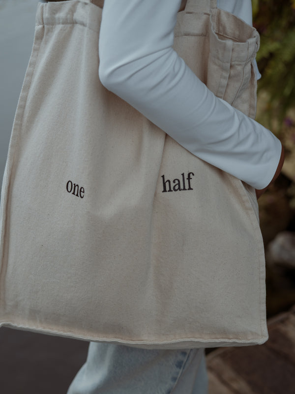 Primer plano de un bolso color crema con texto negro "one half" al hombro de la modelo