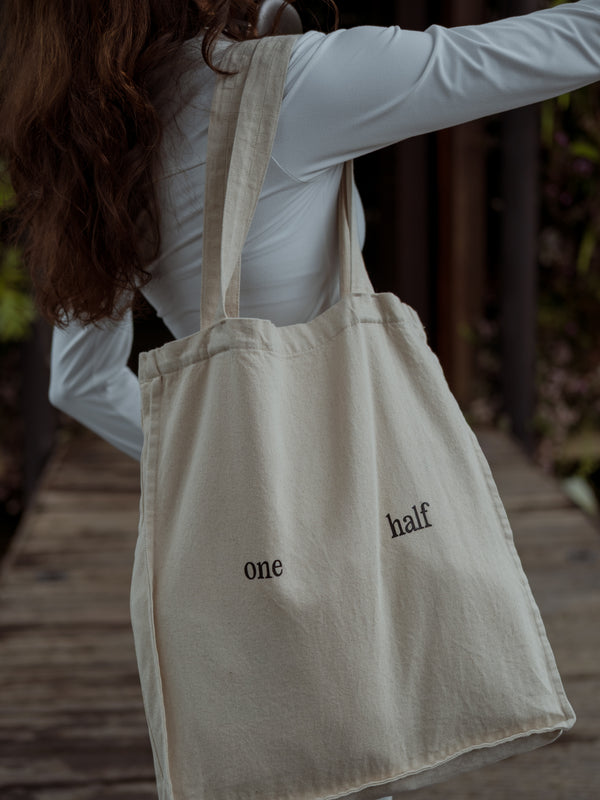 Bolso color crema con texto negro "one half" estampado, colgando del hombro