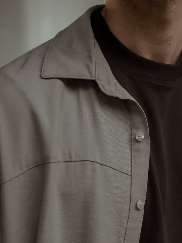 Primer plano de una camisa manga corta color arena sobre una camiseta color café.