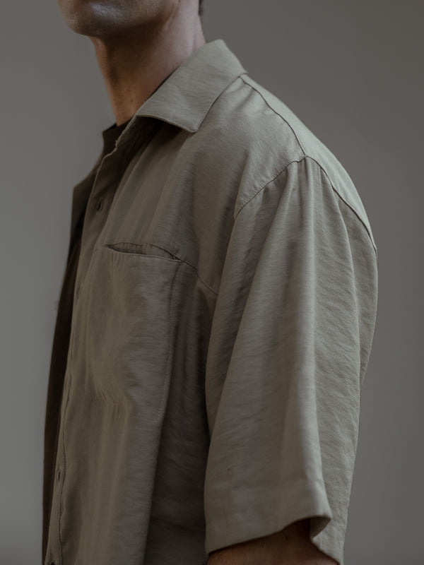 Modelo de perfil, con una camisa manga corta color arena sobre una camiseta color café.