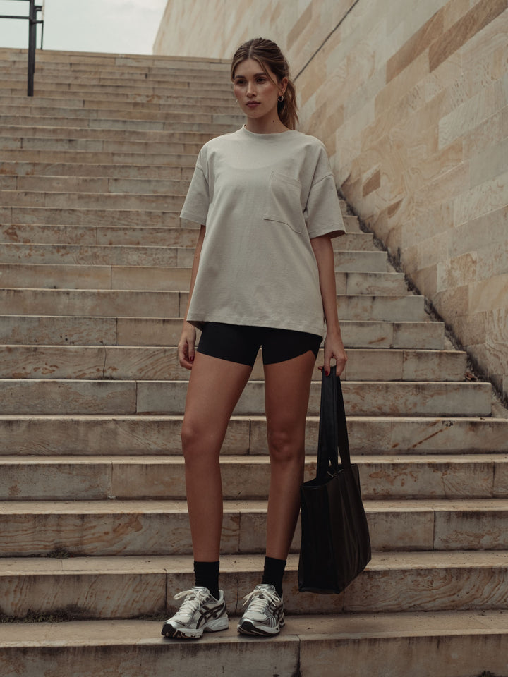 Vista frontal completa de la modelo usando una camiseta color arena, un short y un bolso