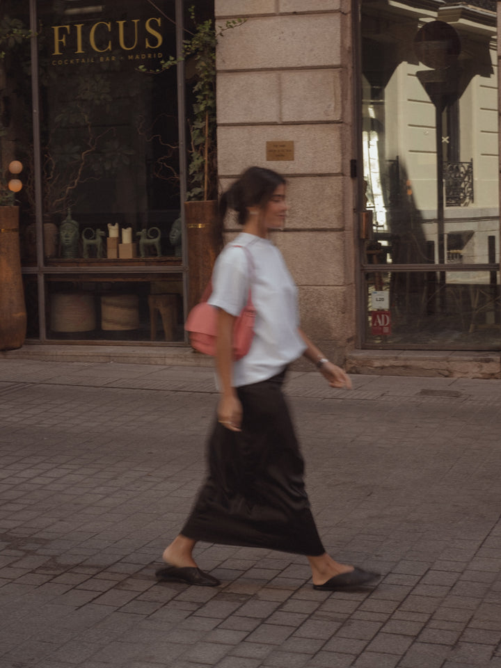 La modelo esta caminando mientras usa una falda larga, una blusa oversized y un bolso 