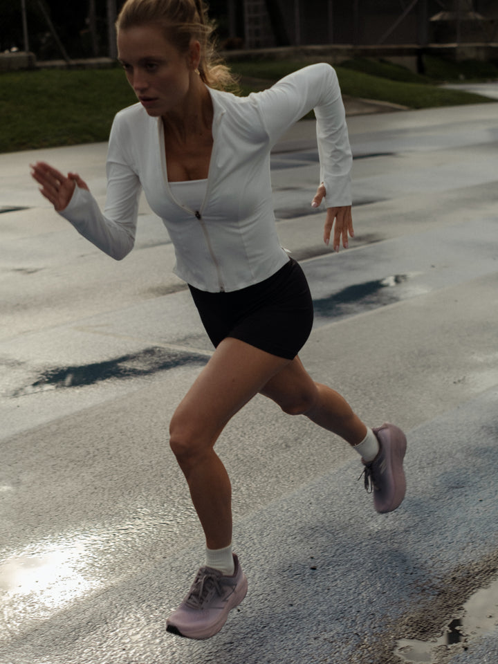 Modelo corriendo usando una chaqueta color crema abierta sobre un top blanco y shorts negros