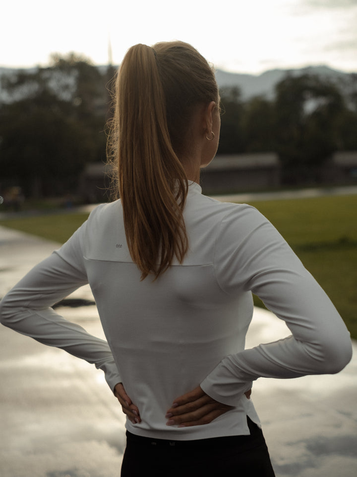 Modelo de espaldas, con las manos en las caderas y usando una chaqueta color crema