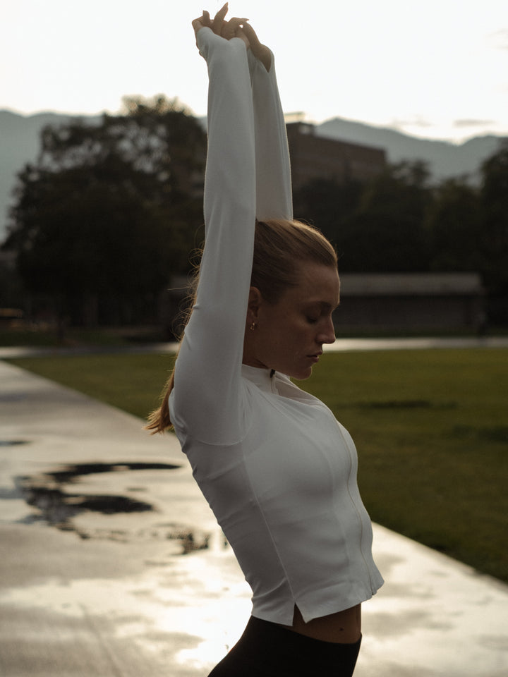 Modelo estirándose, usando una chaqueta color crema y leggings negros 