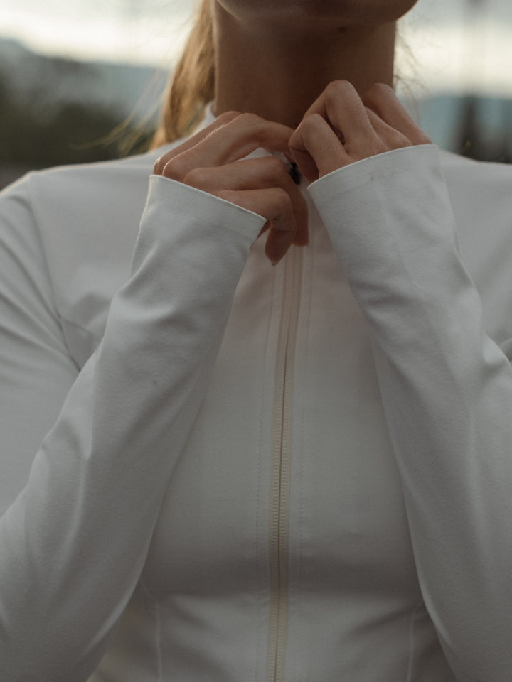 Primer plano de las manos de una modelo cerrando la cremallera de una chaqueta color crema