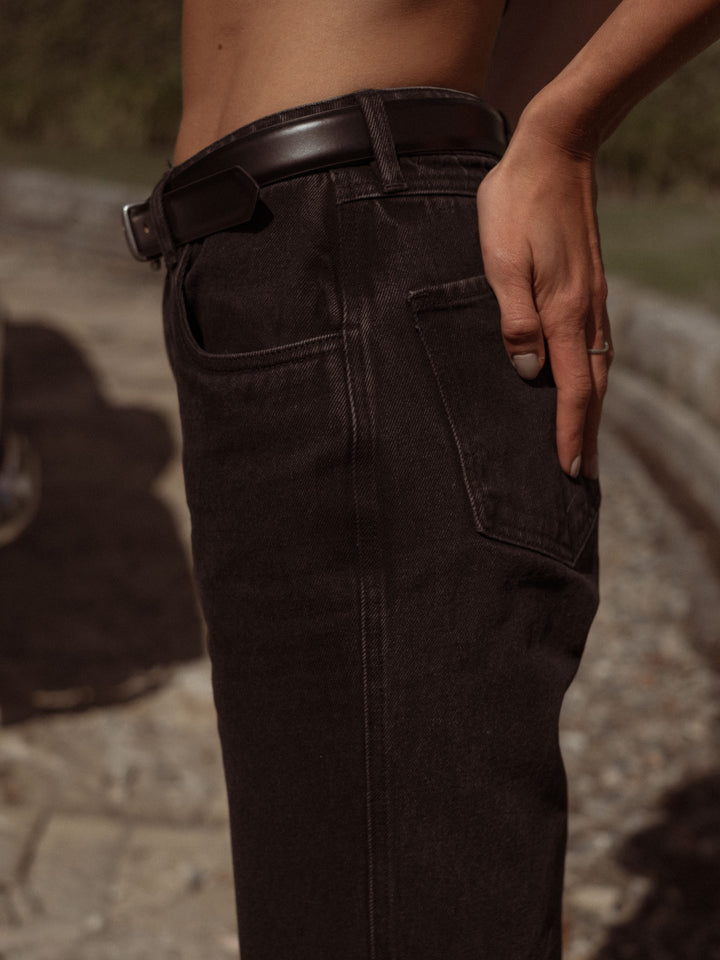 Vista lateral de la modelo usando un jean negro con una correa clásica en cuero negra