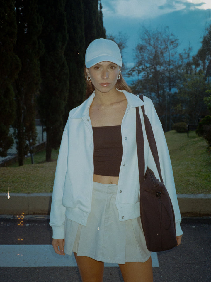 La modelo está usando falda color crema, crop top negro, gorra blanca y chaqueta blanca