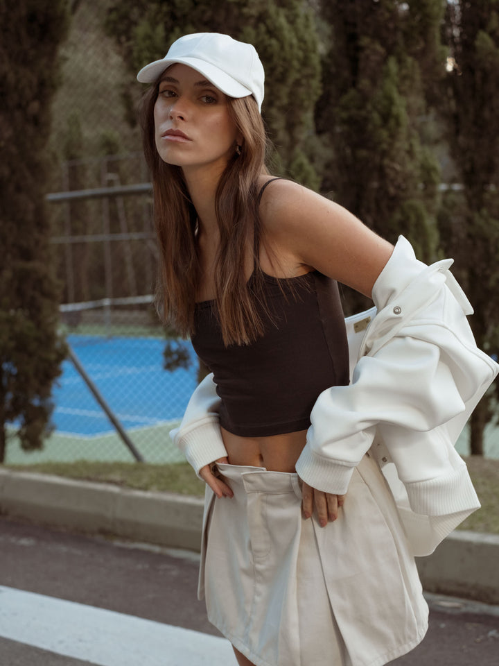 La modelo está usando una gorra blanca, falda blanca, crop top negro y chaqueta blanca