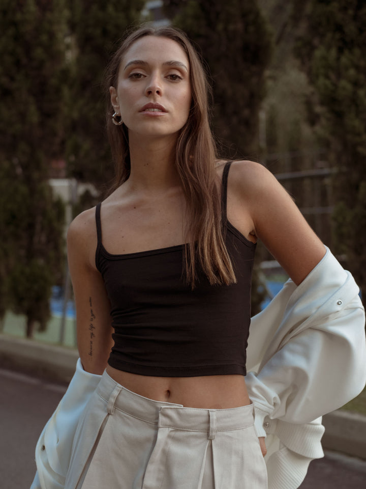 Modelo usando un crop top de tiras negro, falda color crema y chaqueta color blanco