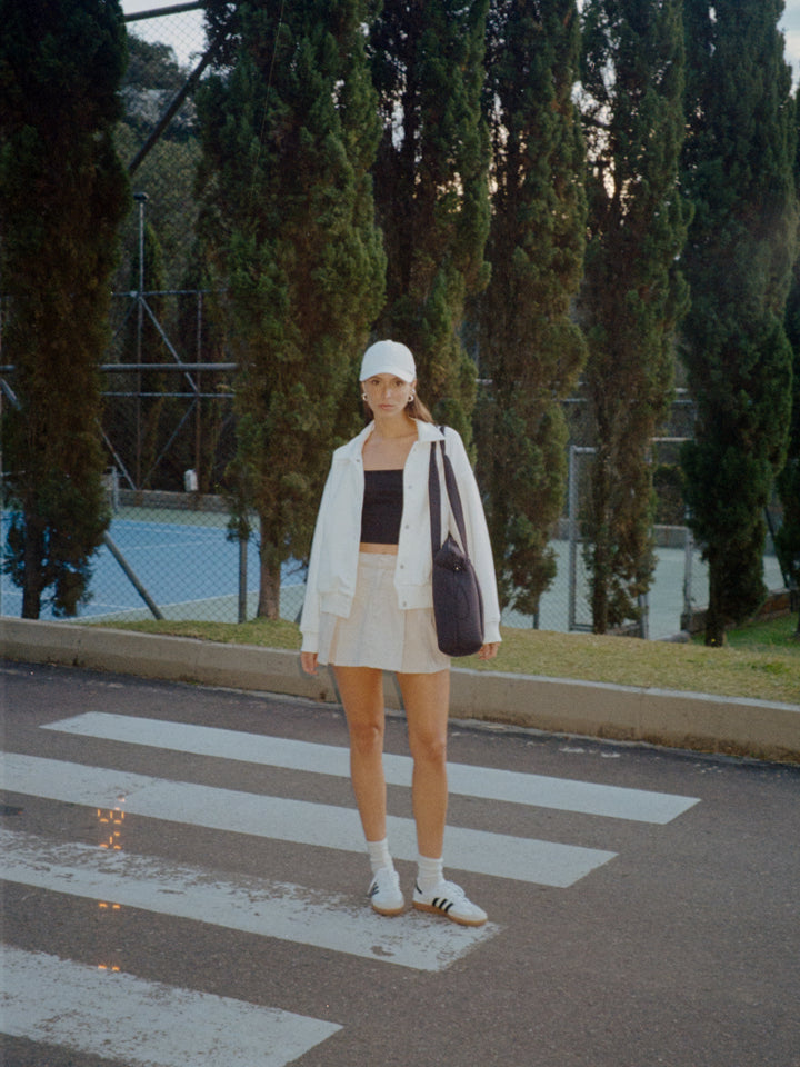 Vista frontal completa de la modelo usando una gorra blanca, crop top negro de tiras, chaqueta blanca, bolso y falda color crema