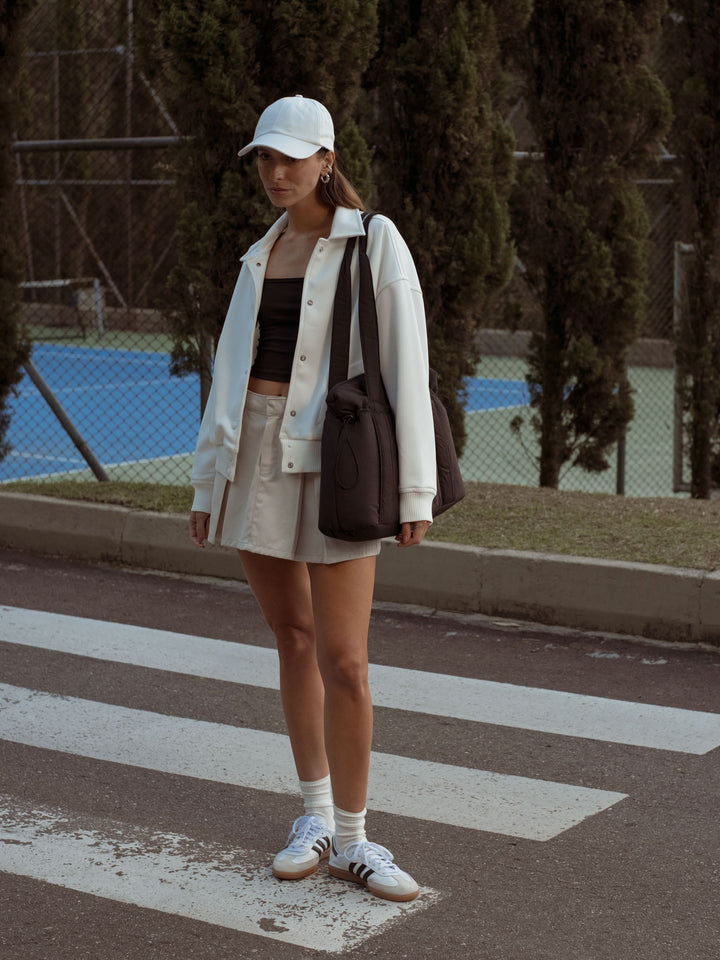 La modelo está usando una gorra blanca, falda blanca, crop top negro y una chaqueta