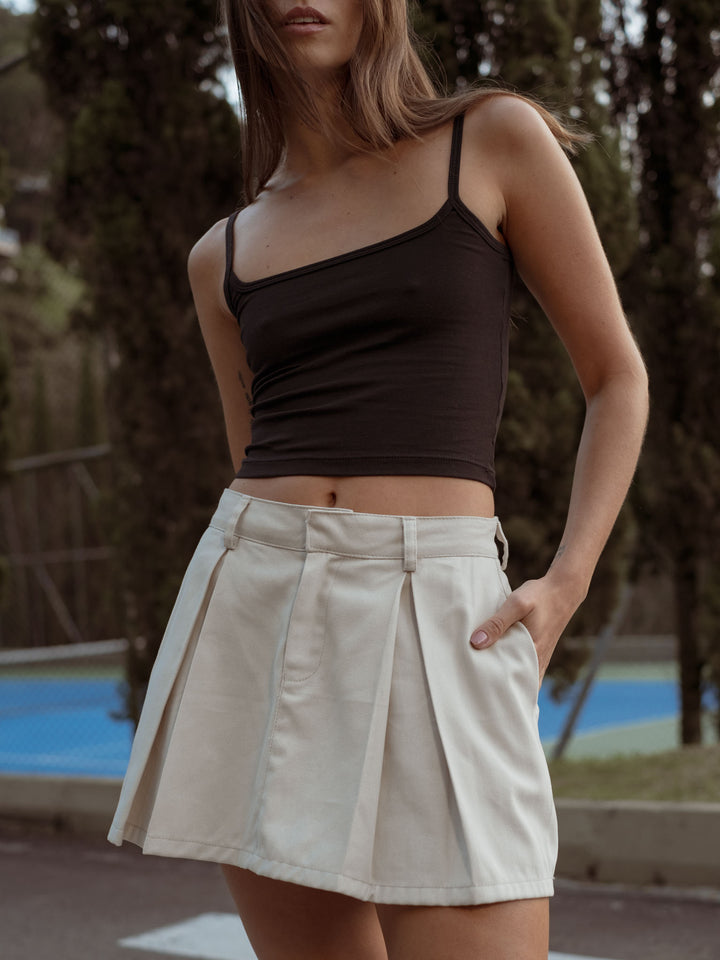 Modelo usando un crop top de tiras color negro y una falda color crudo