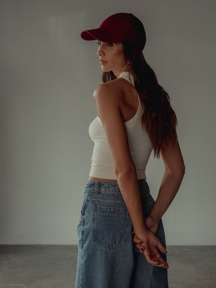 Vista posterior de la modelo usando jean azul, crop top blanco, gorra vino