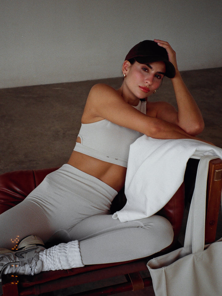 Modelo sentada usando un conjunto deportivo color gris con una gorra color café