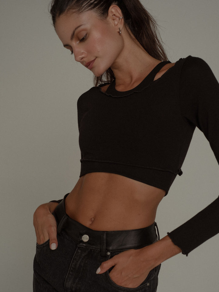 Modelo usando un jean y un crop top manga larga con ruedo al corte color negro
