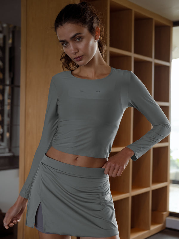 Modelo de pie con una mano en la cadera, usando falda deportiva gris y top manga larga gris