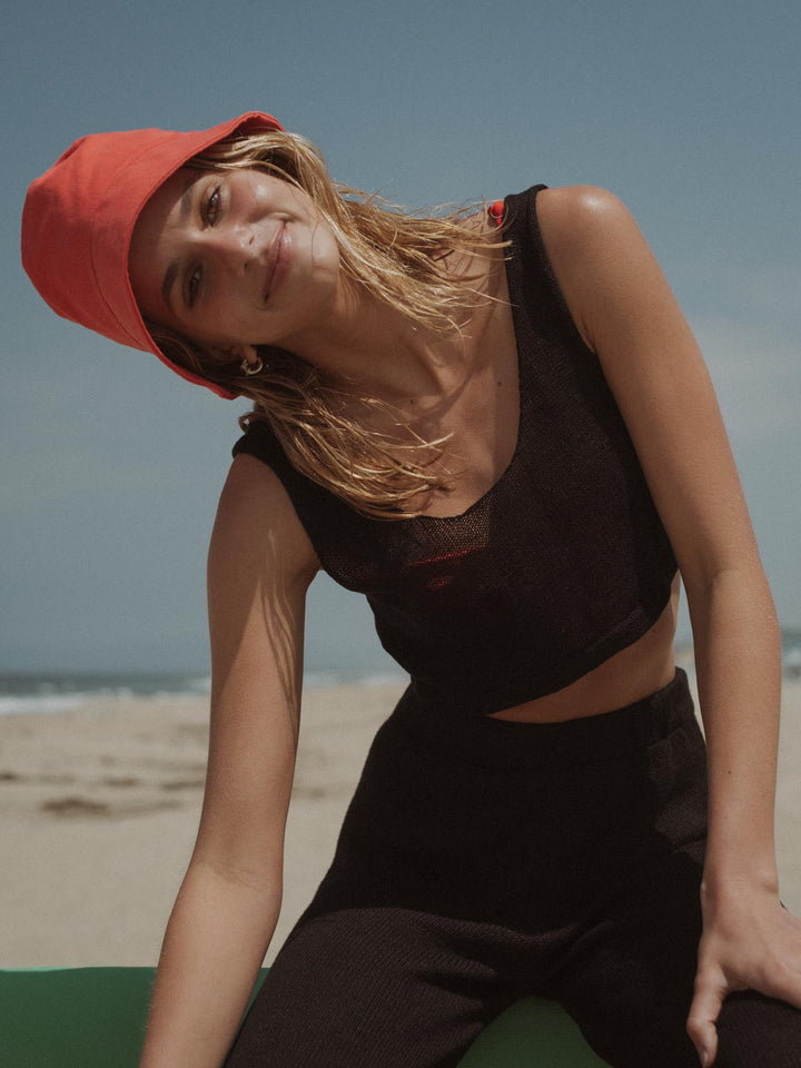 La modelo lleva crop top negro negro, vestido de baño y sombrero rojo