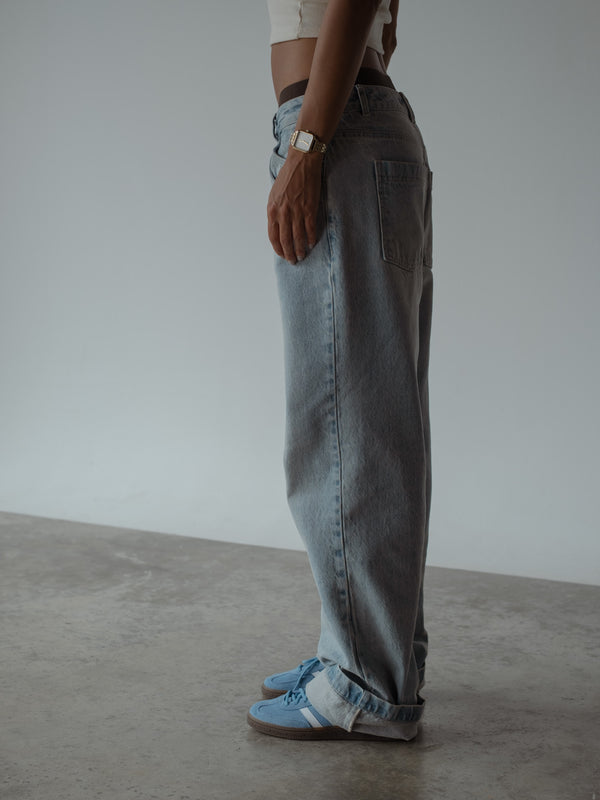 Plano medio lateral de modelo de pie, usando un jean bota recta color azul de tiro medio, combinado con un top corto color crudo.