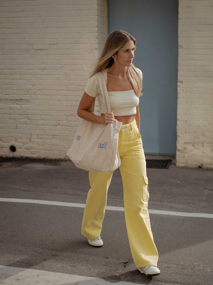 La modelo lleva crop top blanco, jean amarillo y tote bag
