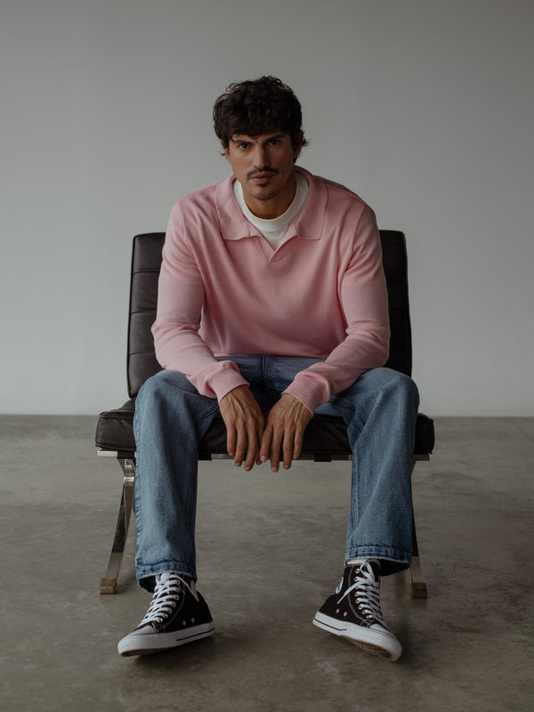 Modelo sentad, usando jean azul de silueta holgada, buzo tipo polo color rosado sobre una camiseta oversized blanca.