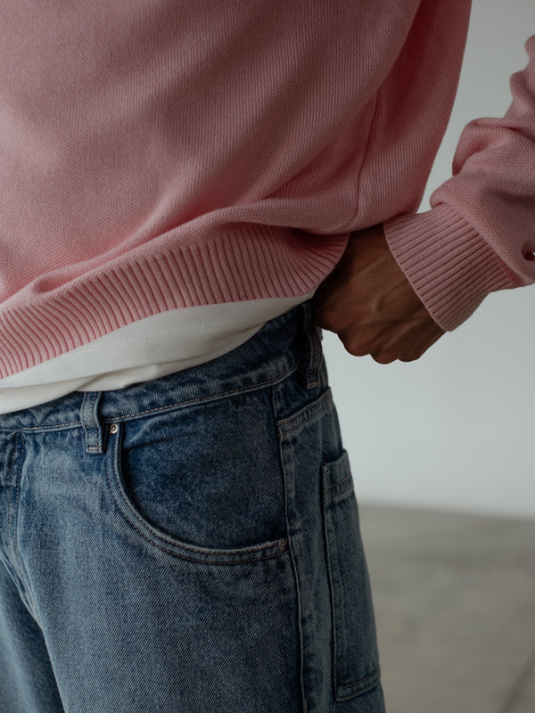 Primer plano de modelo ajustando la pretina del jean azul de bota recta, usando buzo tipo polo color rosado.
