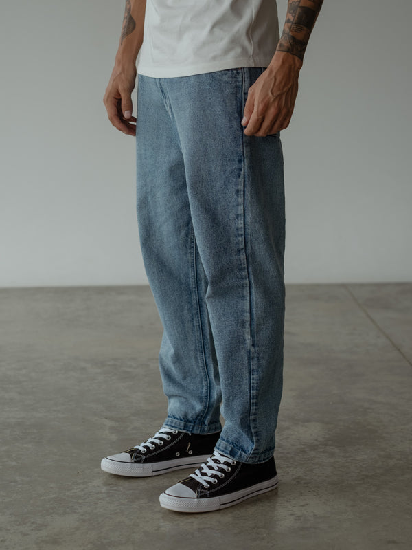 Primer plano de modelo de perfil, con jean azul slim fit y camiseta oversized blanca.