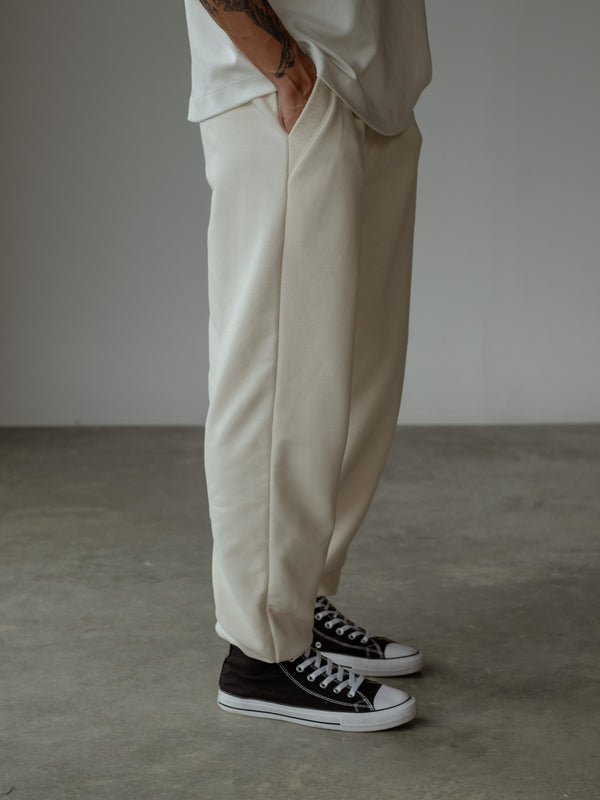 Primer plano de modelo de perfil con la mano en el bolsillo del jogger color crema, usando camiseta oversized color crudo.