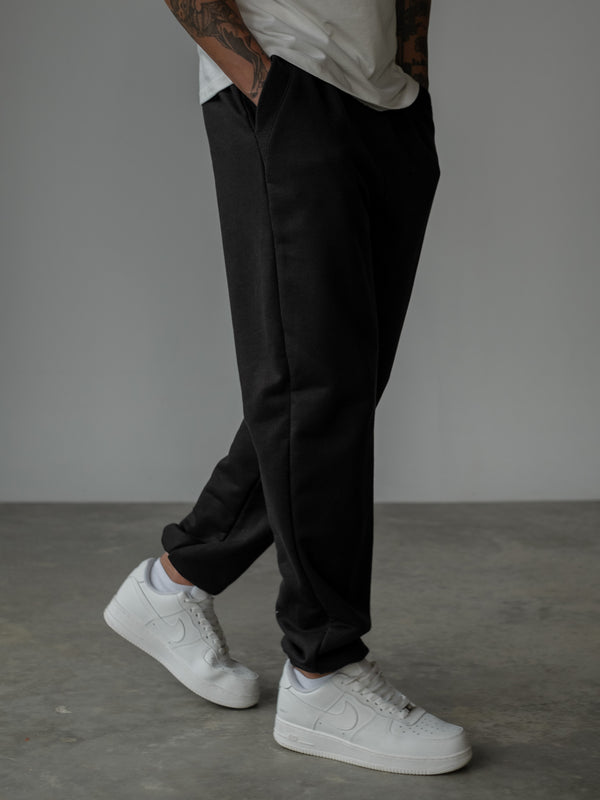 Modelo de pie con las manos en los bolsillos, usando camiseta oversized color crudo y jogger color negro con bota elástica y bolsillos laterales.