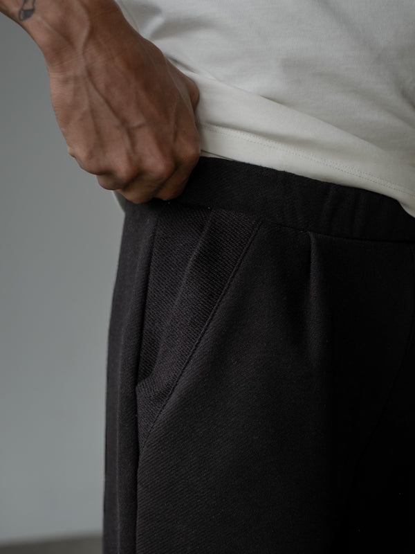 Detalle de la mano de modelo en la pretina enresortada del jogger color negro con bolsillos laterales, usando camiseta oversized color crudo.