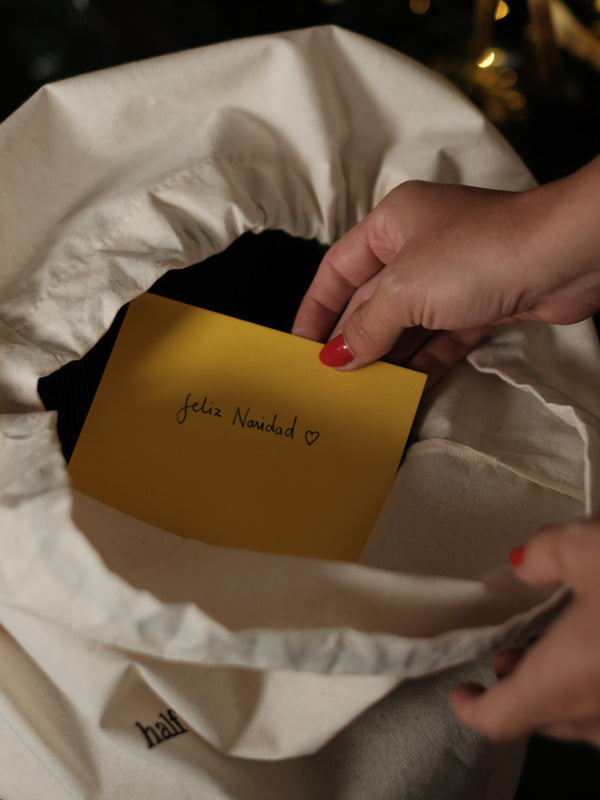 Bolsa de regalo de tela abierta con tarjeta amarilla de "feliz navidad" dentro.