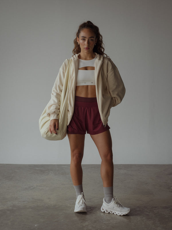 La modelo lleva un top deportivo color crudo, un short color vino, un buzo color crema, un bolso y unas medias largas.