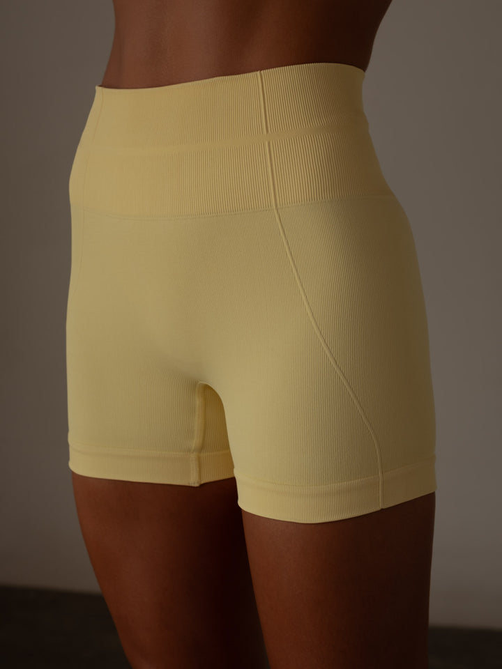 Mini short deportivo color amarillo con pretina acanalada doble y compresión en el abdomen