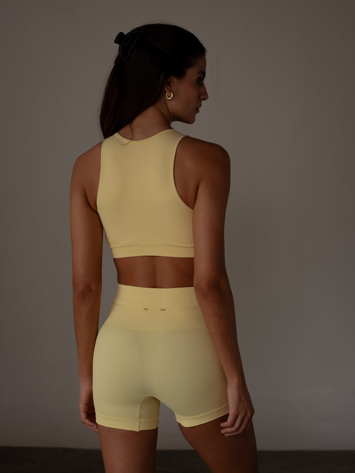 Vista posterior de la modelo usando un mini short color amarillo y un crop top del mismo color 