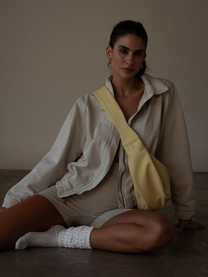 Modelo sentada en el suelo con chaqueta y mini short color gris con un bolso color amarillo