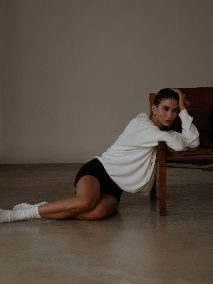 Modelo sentada en el suelo usando un mini short y un buzo color blanco